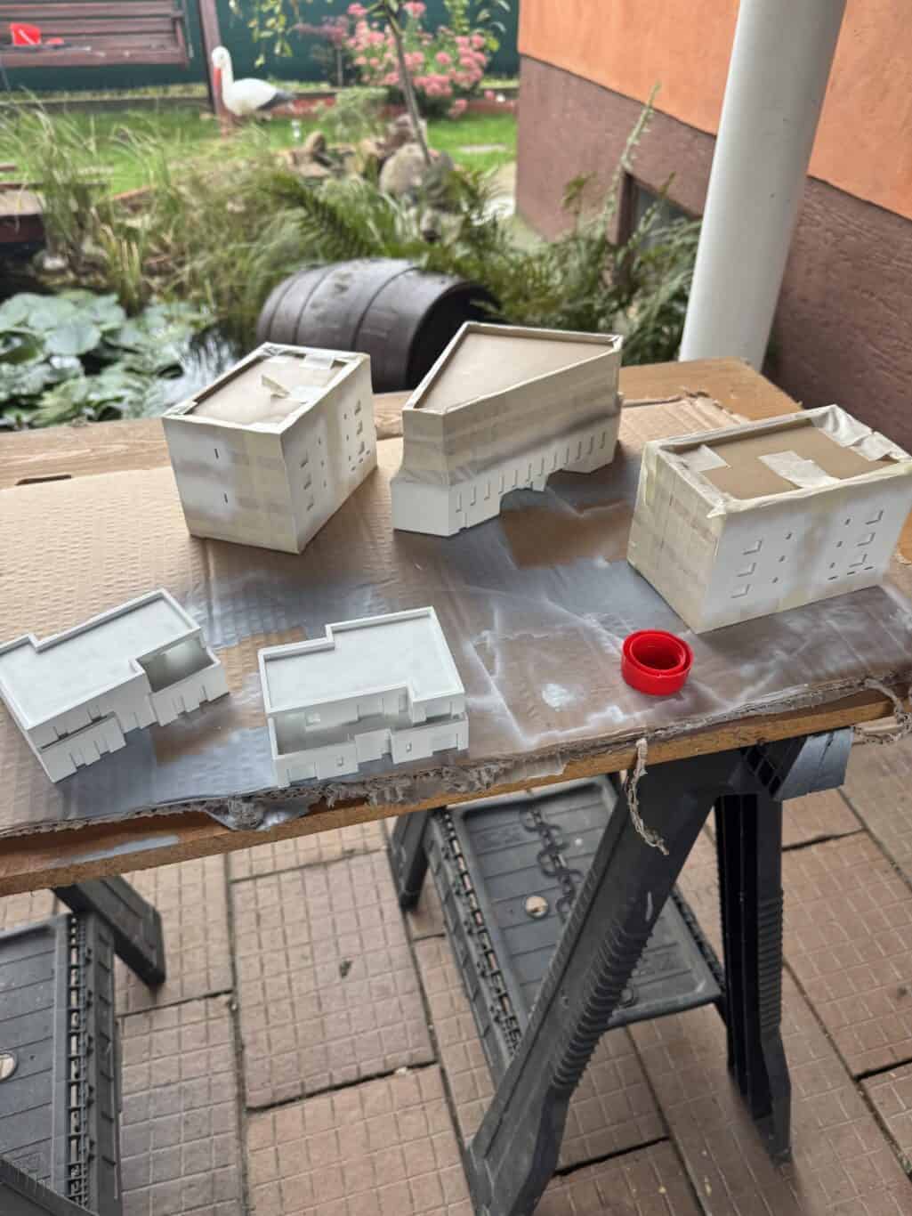 Detail 3D modelov budov na stolíku s modelmi a nástrojmi, príprava na tlač alebo vizualizáciu.